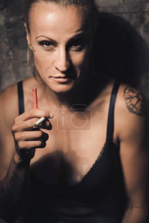 Téléchargez les photos : Femme érotique modèle féminin fumant une cigarette avec ttattoos contre le mur en ville. - en image libre de droit
