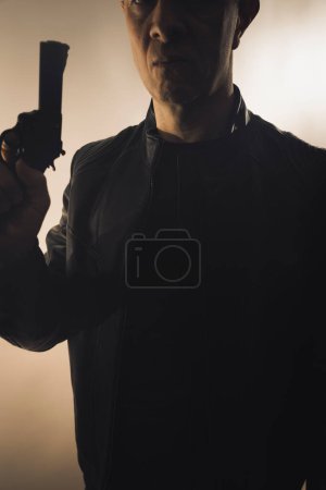 Téléchargez les photos : Détective espion thriller homme avec pistolet photo sombre studio tourné avec éclairage cinématographique. - en image libre de droit