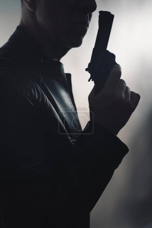 Téléchargez les photos : Détective espion thriller homme avec pistolet photo sombre studio tourné avec éclairage cinématographique. - en image libre de droit