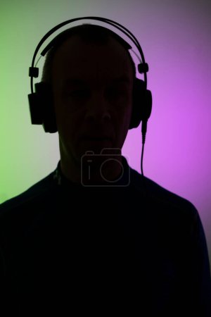 Téléchargez les photos : Dj deejay électronique portant des écouteurs de musique avec des lumières colorées fond studio uni. - en image libre de droit
