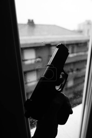 Téléchargez les photos : Gunman tenant le pistolet dans la conception dramatique de couverture de livre photo fenêtre.. - en image libre de droit