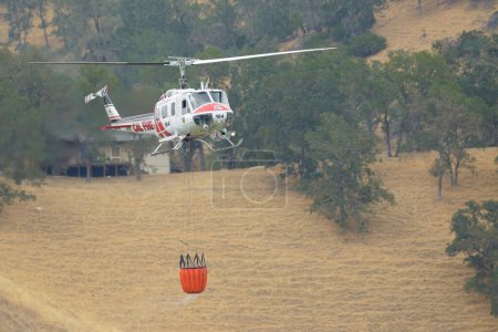 Photo for A Cal Fire Helicopter flying through the hills with a water bucket. Lake Berryessa, California, USA - Royalty Free Image