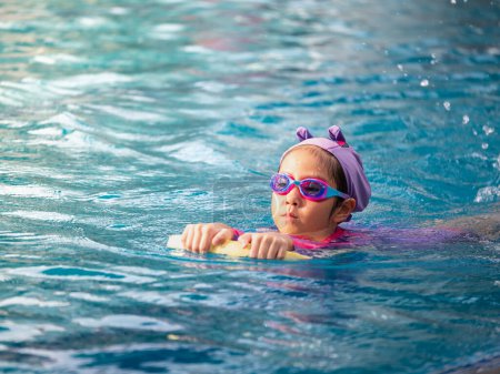 Foto de Niño asiático o niña usando traje de baño para aprender en la piscina, aprender y entrenar nadar en el patinete - Imagen libre de derechos