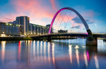Schöne Sunset Clyde Arc Bridge über den Fluss in Glasgow, Schottland, Großbritannien. Es ist schönes Wetter mit Reflexion auf dem Wasser, blauem Himmel, Lichtern von Gebäuden in der Innenstadt, Skyline, Sehenswürdigkeiten. 