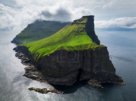 Aerial panorama of a small white lighthouse located on the edge of a huge cliff and the island of Kalsoy. Kalsoy is an isolated small island in the north-east of the Faroe Islands.