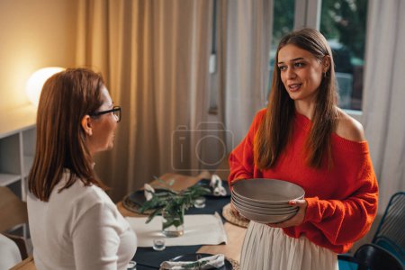 Photo for Female friends preparing dining table for evening dinner party - Royalty Free Image