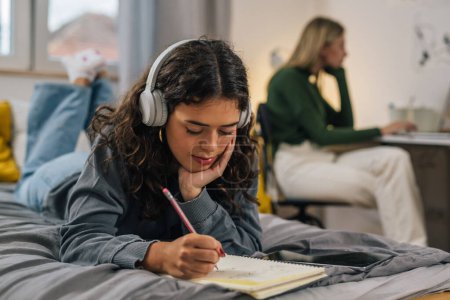 Téléchargez les photos : Étudiante avec casque fait ses devoirs dans un dortoir - en image libre de droit
