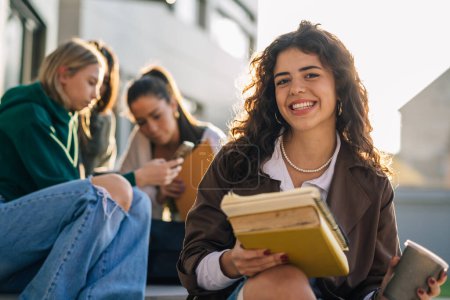 Photo for Portrait of young adult female student smiling and looking at camera outdoor in campus. friends in blurred background - Royalty Free Image