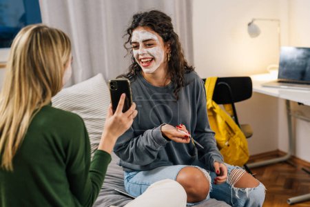 Téléchargez les photos : Amies avec masque de crème cosmétique sur le visage profiter du temps ensemble dans la chambre - en image libre de droit