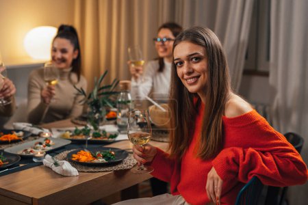 Photo for Young adult woman sitting table on home dinner party holding glass of wine and looking at camera - Royalty Free Image