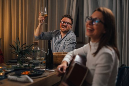 Téléchargez les photos : Amis célébrant chanter et jouer de la guitare à la maison dîner - en image libre de droit
