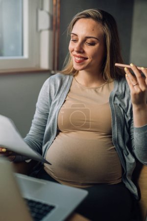 Photo for Pregnant woman looks at papers with a phone in her hand - Royalty Free Image