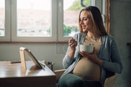 Foto de Mujer embarazada mirando tabletas en casa - Imagen libre de derechos