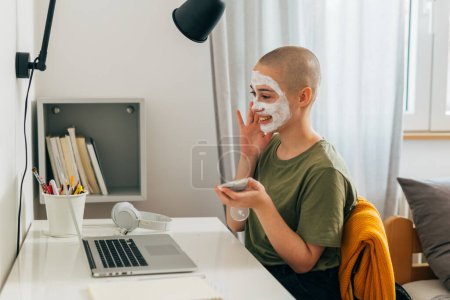 Téléchargez les photos : Une adolescente applique un masque facial devant son ordinateur portable - en image libre de droit