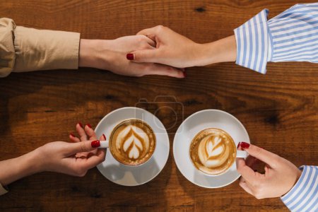 Photo for View from above of holding hands and coffee cups - Royalty Free Image