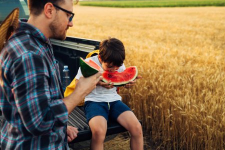 Photo for Son and father eat watermelon in the field - Royalty Free Image