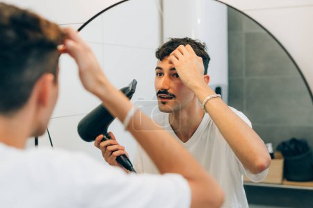 Téléchargez les photos : Jeune homme sèche les cheveux avec sèche-cheveux - en image libre de droit