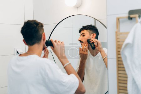 Foto de El joven se afeita la barba con una podadora - Imagen libre de derechos
