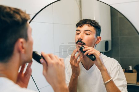 Photo for Man trims his beard in front of a mirror - Royalty Free Image