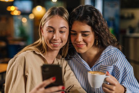 Photo for Front view of two women looking at phone in a cafe - Royalty Free Image