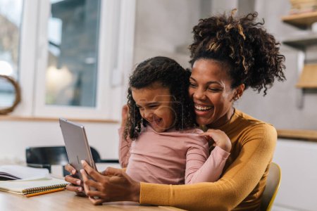 Téléchargez les photos : Maman et fille regardent l'écran de la tablette et rient - en image libre de droit