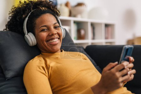 Foto de Mujer alegre escucha música en sus auriculares y mira a la cámara - Imagen libre de derechos
