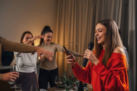 Téléchargez les photos : Femme chante dans le microphone lors d'une fête à la maison, amis dansent - en image libre de droit