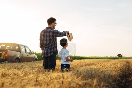 Photo for Father and son are standing in their growing wheat field and enjoying it together - Royalty Free Image