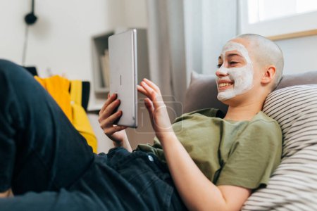 Foto de Mujer joven se acuesta en la cama con una máscara facial y utiliza la tableta - Imagen libre de derechos
