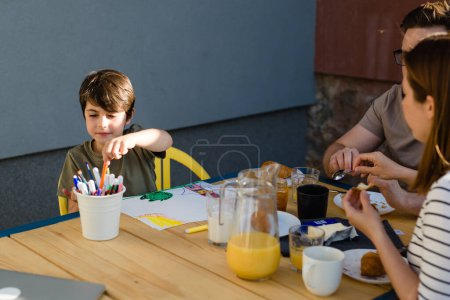 Téléchargez les photos : Garçon assis dehors avec ses parents et dessine - en image libre de droit