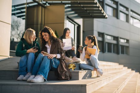 Téléchargez les photos : Les amis de l'université sont assis dans les escaliers devant le bâtiment de l'université par une journée ensoleillée - en image libre de droit