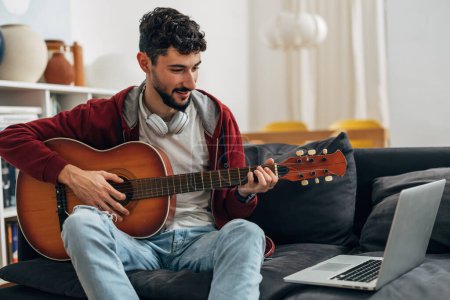 Téléchargez les photos : Jeune homme apprend à jouer de la guitare sur Internet - en image libre de droit
