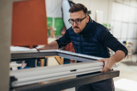 Foto de Hombre de mediana edad trabaja en un taller y produce marcos de ventanas de PVC - Imagen libre de derechos