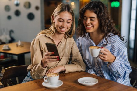 Téléchargez les photos : Deux femmes regardant le téléphone dans un café - en image libre de droit