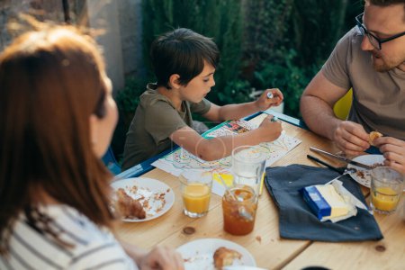 Téléchargez les photos : Garçon dessine dans le jardin tandis que ses parents mangent à côté de lui - en image libre de droit