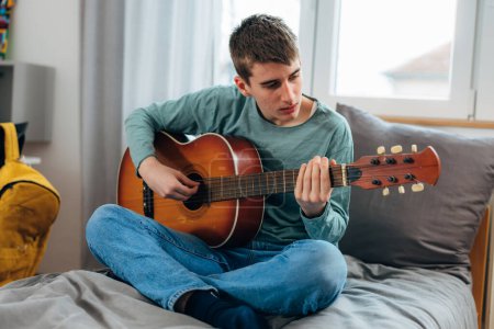 Téléchargez les photos : A teenage boy concentrates on learning how to play guitar - en image libre de droit
