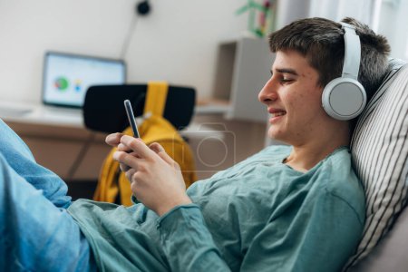 Téléchargez les photos : Adolescent boy with pimples is listening to music using headphones - en image libre de droit