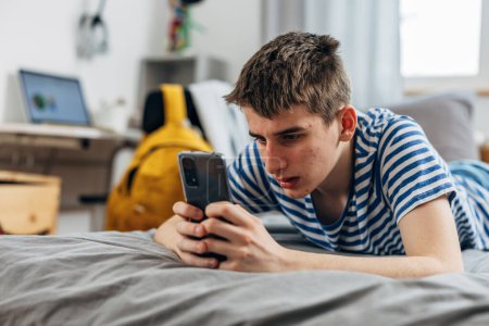 Téléchargez les photos : Teenage boy is surfing on the internet using his phone - en image libre de droit