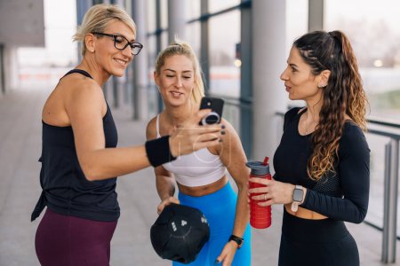 Téléchargez les photos : Three sportswomen look at the phone in the gym - en image libre de droit