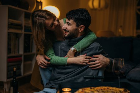 Téléchargez les photos : Smiling woman hugging her boyfriend on the couch from behind in the living room. - en image libre de droit