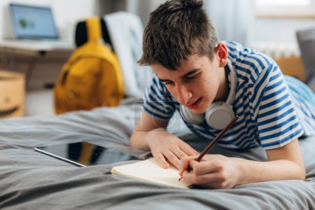 Téléchargez les photos : Teenage boy is doing his homework at home - en image libre de droit