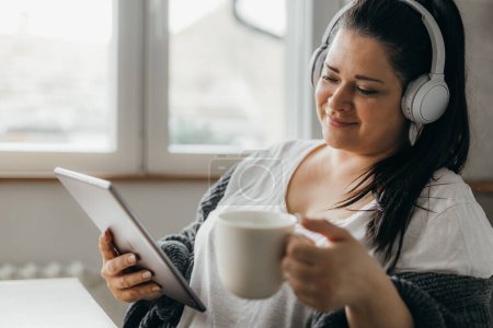 Photo for Beautiful overweight woman enjoys her coffee and uses tablet - Royalty Free Image