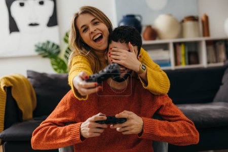 Téléchargez les photos : Woman covers mans eyes while playing a video game together - en image libre de droit