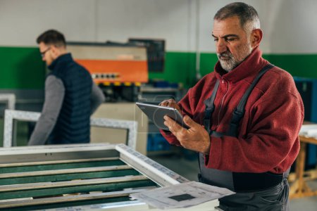 Téléchargez les photos : Senior man works in a PVC industry and looks at the digital tablet - en image libre de droit