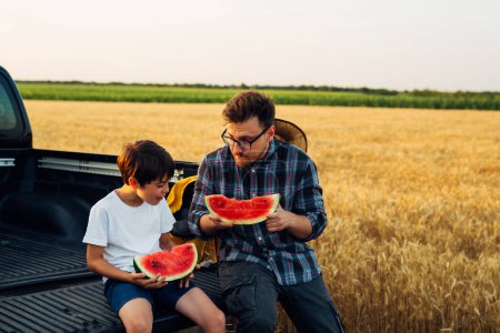 Téléchargez les photos : Boy and his dad eat a watermelon in the field - en image libre de droit