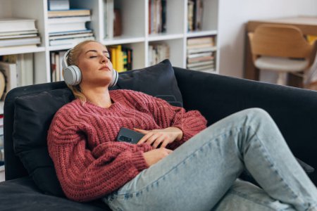 Téléchargez les photos : Caucasian woman is laying on the sofa and listening to enjoyable music - en image libre de droit