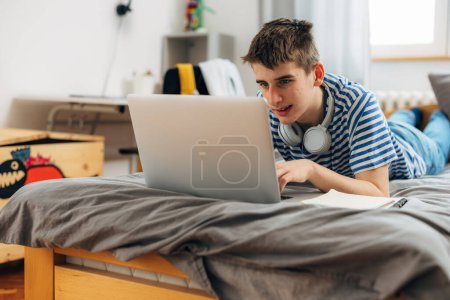 Téléchargez les photos : Adolescent caucasien garçon est ayant un en ligne classe à la maison - en image libre de droit
