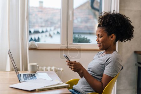 Téléchargez les photos : Side view of an African American woman sitting at home and working remotely - en image libre de droit