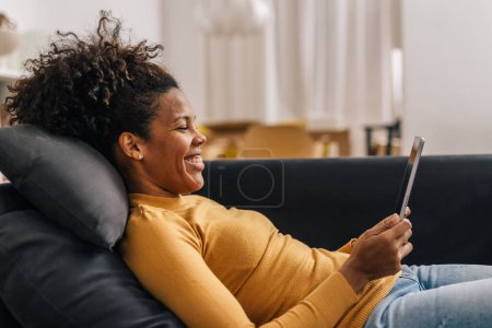 Téléchargez les photos : Side view of a happy mixed race woman using tablet at home - en image libre de droit