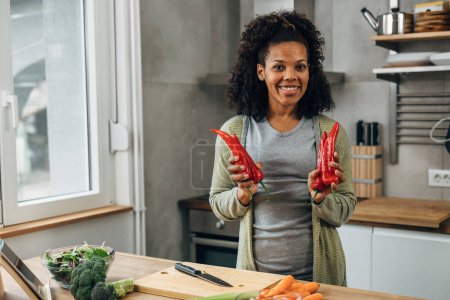 Photo for African American woman is holding red peppers and looking at the camera - Royalty Free Image